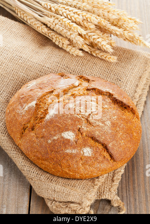 Ganzen Laib frisches Brot mit Ähren auf Sackleinen auf Holztisch Stockfoto