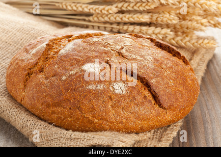 Ganzen Laib frisches Brot mit Ähren auf Sackleinen auf Holztisch Stockfoto