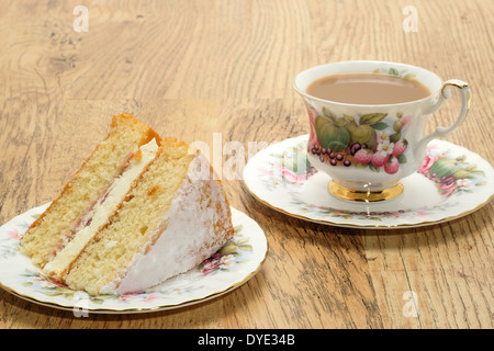 Ein Stück von Victoria Biskuit mit einem heißen Getränk serviert in einem Bone China Tasse und Untertasse Stockfoto