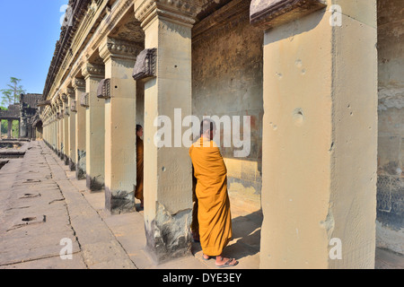 Mönche in Gelb, die im Haupteingang von Angkor Wat, Siem Reap, Kambodscha, zu Besuch sind, die durch die Basreliefs aus der Hinduzeit schlendern Stockfoto