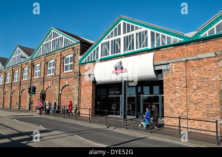 Menschen zu Fuß vorbei an dem Schild & Eingang für das McArthur Glen Designer Outlet Village in Swindon, Wiltshire, UK an einem sonnigen Tag Stockfoto