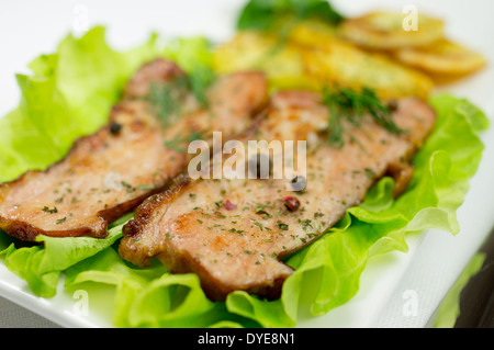 Zwei Stück von gebratenem Speck auf einem Blatt Salat. Scheiben gerösteten Kartoffeln und Petersilie mit Dill und Gewürzen. Stockfoto