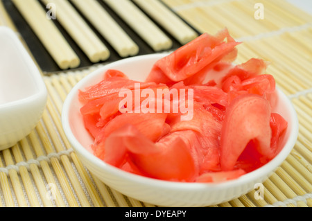 Eingelegten Ingwer in einer Porzellanschüssel. Bambusmatte und Stäbchen auf einem Hintergrund. Stockfoto