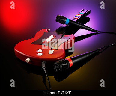 ZWEI MIKROFONE UND EINE GITARRE AUS DEM VIDEOSPIEL GUITAR HERO AUF EINEM ROSA SCHWARZ ROTEN HINTERGRUND Stockfoto