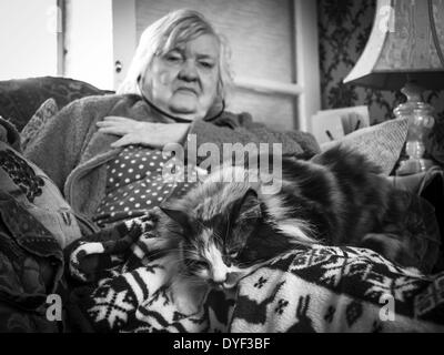 Alte im Alter Dame saß in ihrem Stuhl mit ihrer Katze auf ihrem Schoß und Audio-Handys in ihren Ohren Stockfoto