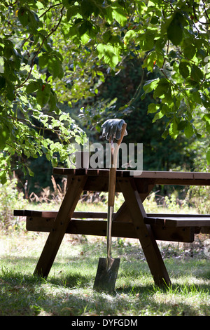 Einen Garten Spaten gegen ein Holztisch mit einem heißen Getränk ausruhen Stockfoto