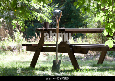 Einen Garten Spaten gegen ein Holztisch mit einem heißen Getränk ausruhen Stockfoto