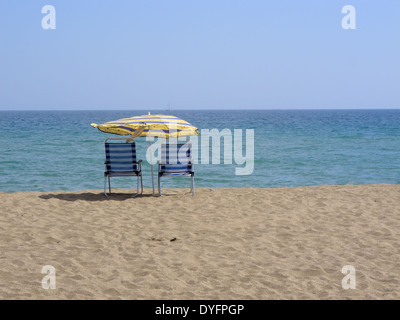 zwei Liegestühle und einen Sonnenschirm am Sandstrand in Spanien Stockfoto