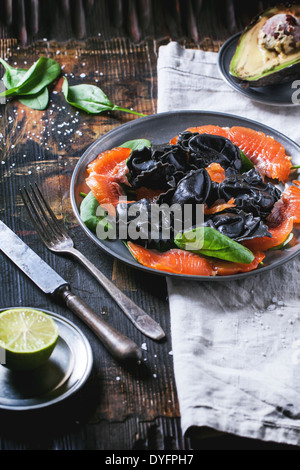 Vintage Platte mit schwarzen hausgemachte Ravioli mit gesalzener Lachs, serviert mit Besteck auf Holztisch. Stockfoto