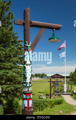 Ein Totempfahl mit Fahnen und Blumen-Garten im Glacier Park Lodge in East Glacier, Montana, USA. Stockfoto