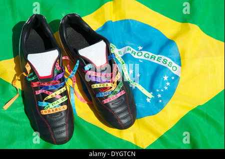 Viel Glück Fußballschuhe Fußball geschnürte mit brasilianischen Wunsch Bändern auf brasilianische Flagge Fußball-Stollen Stockfoto