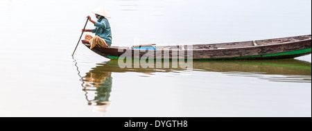 Frau in konische Hut sitzt auf Kanu und Rudern. Traditionelle asiatische Boot aus Holz gebaut. Person Paddel in den Händen halten. Stockfoto