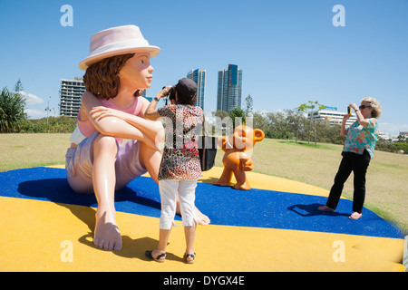 Zwei Touristen fotografieren die riesige Puppe und Teddy Bär an der Gold Coast mit einigen kommerziellen Skyline hinter, März 2014. Stockfoto