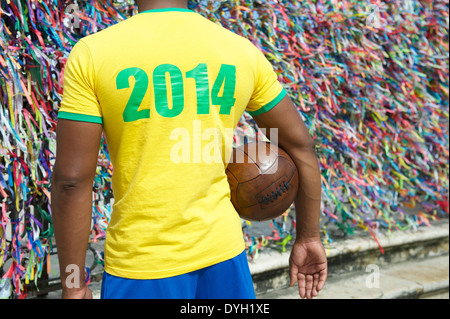 Brasilien 2014 Fußball-Spieler stehen mit Vintage braun Fußball vor Wand des bunten Lembranca Wunsch Bänder in Salvador Stockfoto