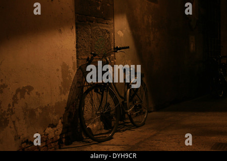 Fahrrad eine Wand in einer Gasse, schwachem Licht mit Schatten von den Straßenlaternen gelehnt. Stockfoto