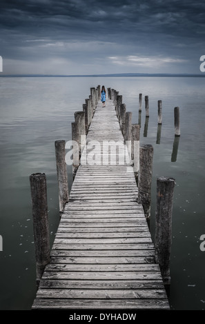 Beängstigend langhaarige Mädchen im blauen Kleid, die zu Fuß auf dem Pier in unheimliche Atmosphäre Stockfoto