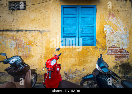 Reihe von Motorräder geparkt in der Nähe von Gebäude mit gelben Grunge Wand. Scooter, Parken in der Straße, Vietnam. Leben in der Stadt mit. Stockfoto