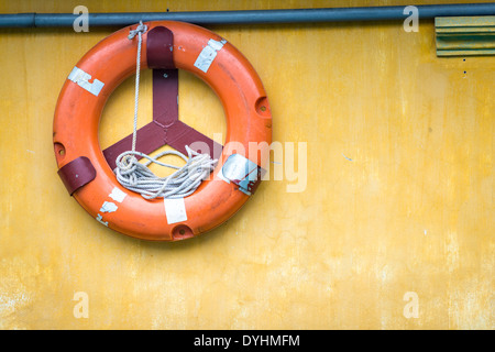Gelbe Wand mit Orangen Boje drauf. Alten Rettungsring mit Seil im Inneren. Ausrüstung für die Rettung der Menschen. Vorsorge für das Überleben. Stockfoto