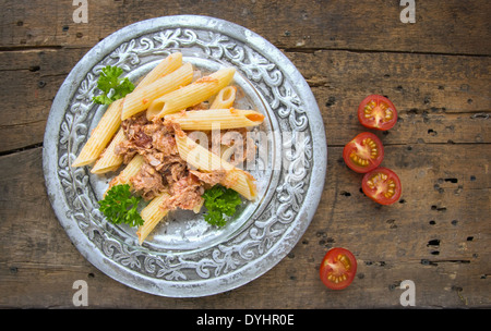 Penne-Nudeln mit Thunfischsauce in Silberplatte auf altem Holz Stockfoto