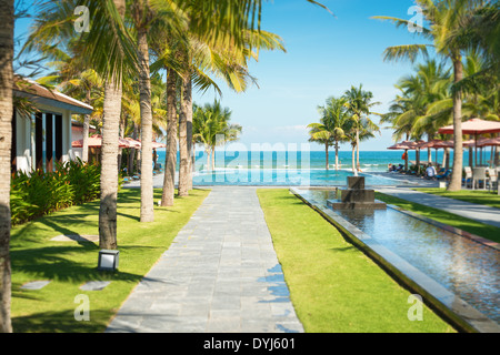 Szene des tropischen Resorts in Vietnam. Schöne Gasse mit Palmen stehen in Reihen, lange Wasserlinie mit kleinen steinernen Brunnen Stockfoto