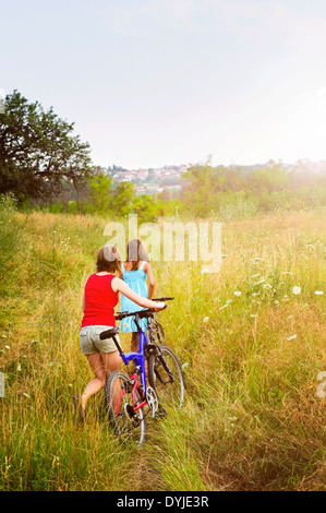 Zwei Mädchen Wandern Fahrräder durch ländlichen Gebiet im Sommer Stockfoto