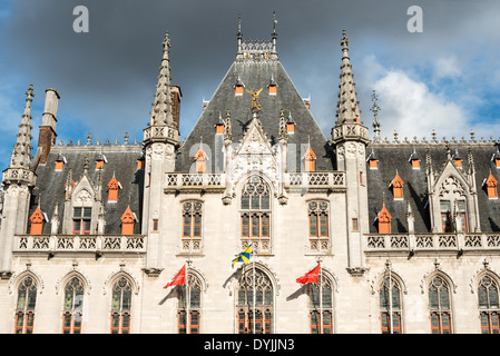 Provincial Court Building Markt Square Brügge Belgien / BRÜGGE, Belgien — das Provincial Court Building überblickt den Markt, das seit dem 10. Jahrhundert das geschäftliche Herz der Stadt ist. Der neogotische Palast wurde von dem Stadtarchitekt Louis Delacenserie und dem Provinzarchitekten René Buyck entworfen und wurde zwischen 1887 und 1921 schrittweise errichtet und ersetzte eine klassizistische Anlage, die 1878 an der Stelle der mittelalterlichen Wasserhalle durch einen Brand zerstört wurde. Die kunstvolle Fassade aus hellem Euville-Stein verfügt über nachgezeichnete Fenster und Giebelgiebeln, die bewusst an das gotische Rathaus von 1376 erinnern, was die Remedievalisierung verstärkt Stockfoto