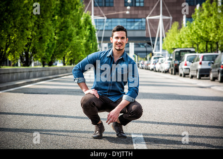 Attraktive lächelnder Mann sitzt in der Mitte der Stadt-Straße, Blick in die Kamera Stockfoto