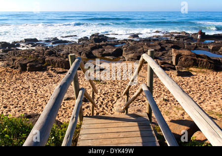 verwitterte Holztreppe führt auf felsigen Strand Stockfoto