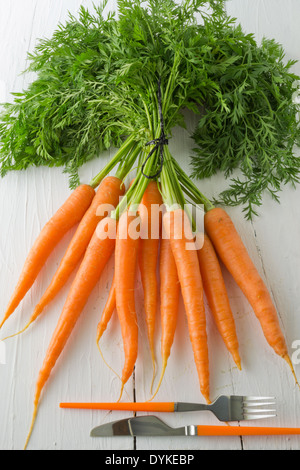 Ein paar Karotten auf einem weißen Tisch mit Messer und Gabel angezeigt. Eine beliebte Wurzel Gemüse voller Vitamin a. Stockfoto