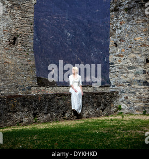 eine Frau in einem weißen Periode Kleid sitzt auf einer Wand in einem Schloss Stockfoto