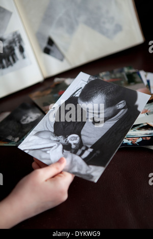 Kind an der Hand hält ein altes schwarz-weiß Foto Mann und Baby ein Familienalbum im Hintergrund entnommen. Stockfoto