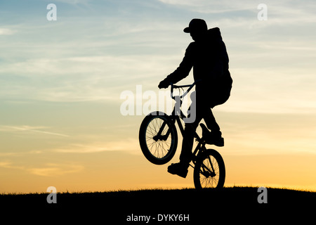 Junger Mann einen Wheelie auf seinem BMX-Fahrrad zu tun. Silhouette Stockfoto
