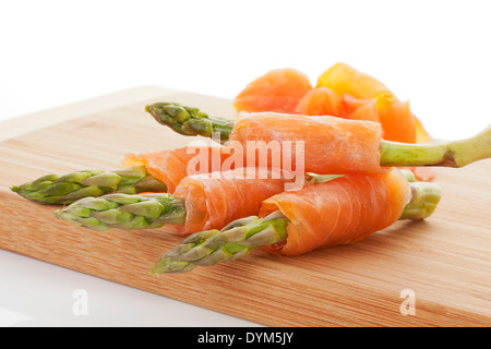 Frischer Spargel und Räucherlachs rollt auf Schneidbrett aus Holz isoliert auf weißem Hintergrund. Gesundes leckeres Essen. Stockfoto