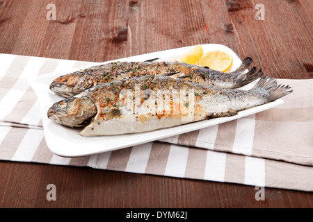 Gegrillte Forelle auf weißen Teller mit Zitrone Stücke auf Küchentuch auf Holztisch. Stockfoto