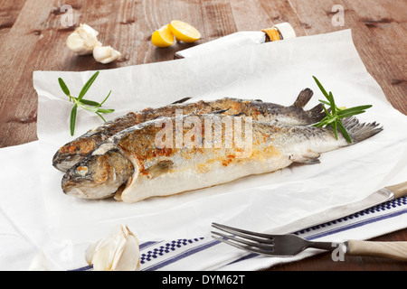 Zwei gegrillte Forelle mit Zitrone, Knoblauch auf Backpapier auf Küchentuch auf Holztisch weiß. Stockfoto