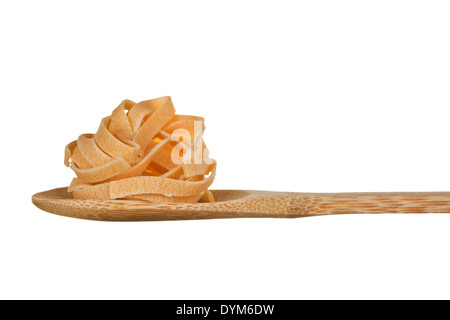 Trockene Nudeln auf Holzlöffel. Rohe Tagliatelle auf hölzernen Esslöffel vor weißem Hintergrund. Stockfoto