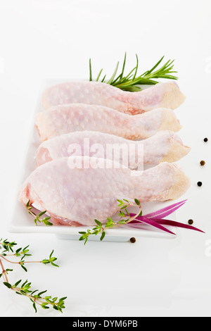 Hähnchenschenkel auf weißen Teller auf weißem Hintergrund mit Pfefferkörnern und frischen Kräutern dekoriert. Stockfoto