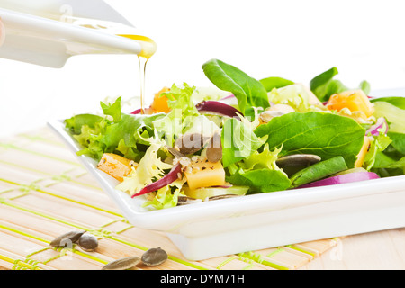 Gießen Olivenöl Dressing auf frischen Ziegenkäse Salat in weißen Teller. Stockfoto