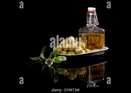 Olivenöl in Flasche und frischen Oliven in schwarz Schüssel auf schwarzem Hintergrund mit frischen Olivenblättern isoliert. Luxuriöse kulinarische Speisen Stockfoto