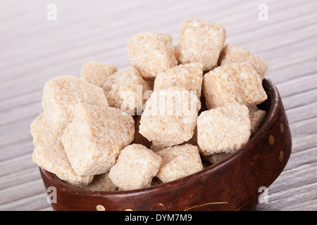 Brauner Zucker Würfel Detail in Runde Holzschale auf braunem Hintergrund. Kulinarischer Zucker Hintergrund in braun. Stockfoto