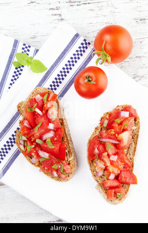 Leckere Bruschetta auf dem weißen Tuch auf weißem Holz Hintergrund mit frischen Kräutern und Tomaten. Kulinarisches Essen. Stockfoto