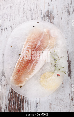 Gefrorenen Fischfilet mit frischen Kräutern und Zitrone auf weißen hölzernen strukturierten Hintergrund. Kulinarischen Meeresfrüchte essen. Stockfoto