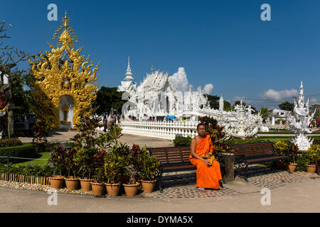 Mönch sitzt vor dem reich verzierten goldenen Eingang des Wat Rong Khun, weiße Tempel, von dem Architekten Chalermchai Kositpipat Stockfoto