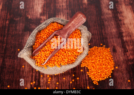 Rote Linsen in Leinensack auf Holzlöffel auf dunklem Holz, Ansicht von oben. Gesunde Ernährung. Stockfoto