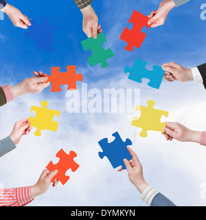 Kreis der Menschen Hände mit verschiedenen Puzzleteile mit blauem Himmel und weißen Wolken Hintergrund Stockfoto