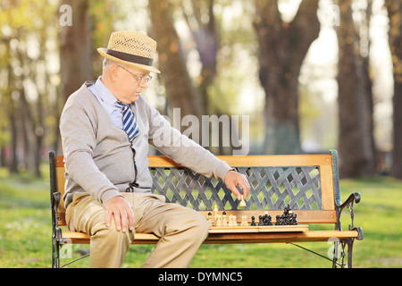 Alter Mensch Schach allein im Freien sitzen auf Holzbank Stockfoto