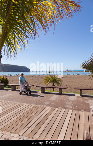 Tourist mit walking Frame ein Spaziergang auf der Strandpromenade Promenade in Los Cristianos, Teneriffa, Kanarische Inseln, Spanien. Stockfoto