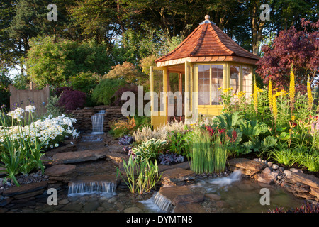 Ein Land Vorstadtgarten im Sommer mit einem Sommerhaus Sommerhaus Hütte kleinen Teich Wasserspiel mit Wasserfall und bunte Blumen gemischt Grenze Großbritannien Stockfoto