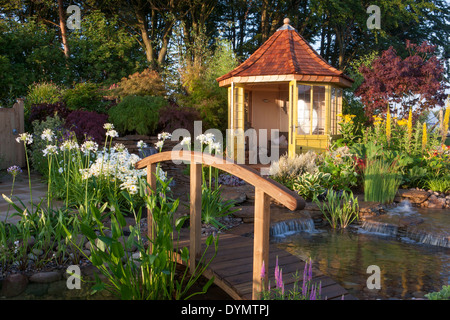 Ein Garten auf dem Land im Sommer mit einer Brücke über das Sommerhaus Sommerhaus Hütte kleinen Teich Wasser Feature Wasserfall eine gemischte bunte Blume Grenze Großbritannien Stockfoto