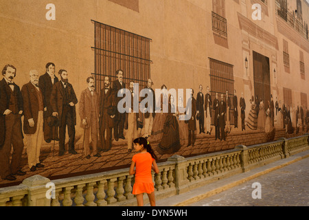 Kubanischen Mädchen in orange zu Fuß durch eine gemalte Wandbild der intellektuellen Oberschicht der Kolonialzeit in Alt-Havanna-Kuba Stockfoto